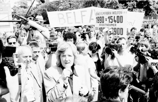Birgit Breuel, 1991–1994 Präsidentin der Treuhandanstalt, bewegte sich stets in einem Spannungsfeld zwischen den Erwartungen von Politik, Öffentlichkeit und Belegschaften sowie ihren eigenen ordnungspolitischen, betont marktliberalen Grundüberzeugungen, die sie seit den 1970er-Jahren verfochten hatte. Bei dieser Protestkundgebung vor der Berliner Treuhand-Zentrale im Juni 1992, abgehalten von der »Konferenz ostdeutscher und Berliner Betriebsräte«, warb Breuel gegenüber Journalisten offensiv für den von der Treuhand eingeschlagenen Kurs forcierter Massenprivatisierungen. Generell war der Platz vor der Treuhand-Zentrale (dem früheren Reichsluftfahrtministerium der NS-Zeit bzw. dem ehemaligen Haus der Ministerien der DDR) Anfang der 1990er-Jahre ein beliebter Ort für Demonstrationen. (ddrbildarchiv.de, Foto: Burkhard Lange)