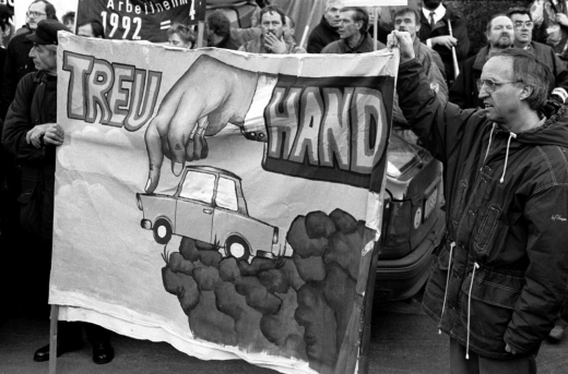 Im Dezember 1992 zeigte dieser Demonstrant ein aufwendig gestaltetes, treuhandkritisches Protestbanner mit charakteristischer (Treu-)Hand-Ikonographie nebst Anzug und Manschettenknöpfen, welches den Untergang der einstigen DDR-Automobilindustrie anprangerte. Deren weitgehende »Abwicklung« hatte der Treuhand-Vorstand um Detlev Rohwedder im Frühjahr 1991 beschlossen, mit Verweis auf die desolate Markt- und Wettbewerbssituation. Die bundesdeutschen Fahrzeugbauer hatten eine Übernahme der alten Produktionsstätten in Zwickau (Trabant) oder Eisenach (Wartburg) verworfen und sich stattdessen für Neuansiedlungen entschieden (ddrbildarchiv.de, Foto: Burkhard Lange)
