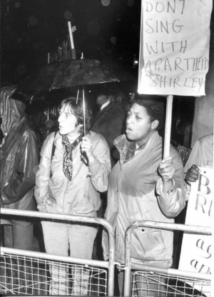 Demonstranten fordern von der Sängerin Shirley Bassey, Tochter einer englischen Mutter und eines nigerianischen Vaters, sich gegen die Apartheid auszusprechen. Die Protestaktion fand im November 1982 vor Basseys Konzert in Cardiff statt, wo die Künstlerin in einem multiethnischen Stadtteil aufgewachsen war. 1981 und 1982 war Bassey mehrfach im südafrikanischen Sun City aufgetreten und hatte damit gegen den Kulturboykott verstoßen. (AAM Archives Committee; unbekannter Fotograf)