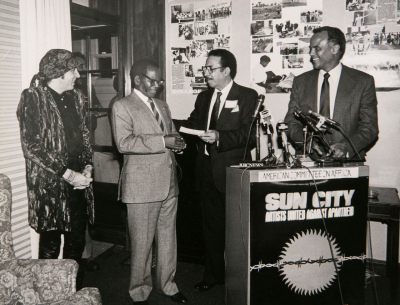 Das American Committee on Africa und der Africa Fund empfangen den ANC-Präsidenten Oliver Tambo 1987 in New York. Tilden LeMelle, Vorsitzender des Africa Fund, überreicht Tambo einen Scheck über 100.000 Dollar, eine erste Tranche aus dem Erlös des Sun-City-Albums, das insgesamt mehr als eine Million Dollar für wohltätige Zwecke einbrachte. Rechts Harry Belafonte, links Steven Van Zandt. Siehe auch das Tondokument unter <http://africanactivist.msu.edu/audio.php?objectid=32-12E-1>. (African Activist Archive Project; Foto: David Vita)