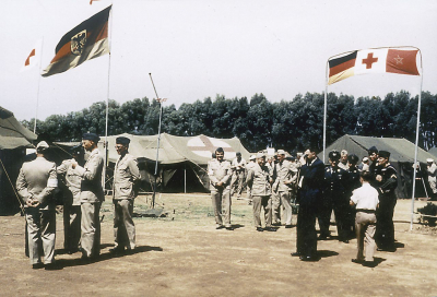 Deutsche Uniformen im Ausland: Erdbebenhilfe für Agadir/Marokko 1960. Bundeswehrsoldaten, teilweise in der wegen der Hitze nachgelieferten »Tropenuniform«, warten auf eine marokkanische Delegation, der sie nach Abschluss des Einsatzes den Hauptverbandplatz als Geschenk übergeben. Das improvisierte Banner, das über ein rotes Kreuz die bundesdeutsche und die marokkanische Fahne verbindet, zeigt an, dass sich die Soldaten ihrer Funktion im Dienst der Völkerverständigung bewusst waren. (© Redaktion der Bundeswehr. Mediendatenbank)
