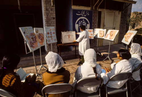 Vortrag zur Familienplanung in Lahore, Pakistan, ca. 1973. Um die Geburtenrate zu reduzieren, hatte die pakistanische Regierung die Vereinten Nationen um Unterstützung gebeten. Bei den gesundheitsökonomischen Beratungs- und Forschungsleistungen wirkten verschiedene Unterorganisationen zusammen: United Nations Fund for Population Activities (UNFPA), World Health Organization (WHO), United Nations Children’s Fund (UNICEF), United Nations Educational, Scientific and Cultural Organization (UNESCO) sowie International Labour Organization (ILO). (United Nations Photo 380444/B. Wolff)