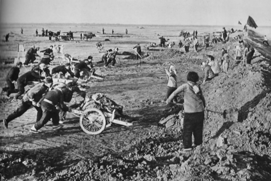 Arbeitseinsatz beim Deichbau, Nordchina, 1960er-Jahre. Im Hintergrund ist links ein aufgestelltes Mao-Bild zu erkennen. (aus: Die rote Sonne erhellt den Weg, auf dem Dadschai vorwärtsschreitet, Peking 1969, S. 131. Solche deutschsprachigen Propaganda-Publikationen richteten sich an eine eingeschränkte Öffentlichkeit in der DDR, vor allem aber an ein Publikum in Westdeutschland, Österreich und der Schweiz.)