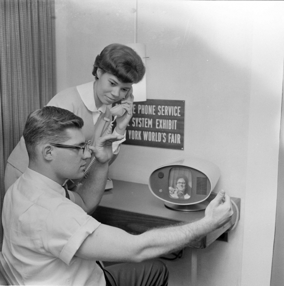 Das Foto zeigt – idealisiert – die Verständigung in Amerikanischer Gebärdensprache (<em>American Sign Language</em>, ASL) mithilfe der in den 1960er-Jahren noch neuen Technik der Bildtelefonie. Ein Student führt hier auf der New Yorker Weltausstellung 1965 ein solches Gespräch am Stand des Herstellers. Abbildungen wie diese machen auf Innovationen der Hilfsmitteltechnik aufmerksam, sagen aber nichts über deren Verbreitung und Zugänglichkeit aus. Solche Fotos zeigen technizistische Fortschrittsversprechen, die kritisch zu hinterfragen sind. Selbst in den USA waren derartige Bildtelefone kaum verbreitet. In Deutschland gab es fast gar keine. Selbst die in den 1970er-Jahren käuflichen Schreibtelefone besaßen nur wenige Privathaushalte. Technik dieser Art erleichtert Menschen mit Hörbehinderungen die Kommunikation nur dann, wenn ihr Gegenüber ebenfalls darüber verfügt. Das war bei Bild- und Schreibtelefonen aber nicht der Fall, nicht einmal bei öffentlichen Stellen oder Behörden. Erst flächendeckend verfügbare Faxgeräte, die SMS-Funktion von Handys sowie später die Messenger-Apps und Videochats erweiterten wirklich die Kommunikationsmöglichkeiten sowohl für Gebärdensprachen als auch für Schriftsprachen. (picture-alliance/AP Images) Das Foto zeigt – idealisiert – die Verständigung in Amerikanischer Gebärdensprache (<em>American Sign Language</em>, ASL) mithilfe der in den 1960er-Jahren noch neuen Technik der Bildtelefonie. Ein Student führt hier auf der New Yorker Weltausstellung 1965 ein solches Gespräch am Stand des Herstellers. Abbildungen wie diese machen auf Innovationen der Hilfsmitteltechnik aufmerksam, sagen aber nichts über deren Verbreitung und Zugänglichkeit aus. Solche Fotos zeigen technizistische Fortschrittsversprechen, die kritisch zu hinterfragen sind. Selbst in den USA waren derartige Bildtelefone kaum verbreitet. In Deutschland gab es fast gar keine. Selbst die in den 1970er-Jahren käuflichen Schreibtelefone besaßen nur wenige Privathaushalte. Technik dieser Art erleichtert Menschen mit Hörbehinderungen die Kommunikation nur dann, wenn ihr Gegenüber ebenfalls darüber verfügt. Das war bei Bild- und Schreibtelefonen aber nicht der Fall, nicht einmal bei öffentlichen Stellen oder Behörden. Erst flächendeckend verfügbare Faxgeräte, die SMS-Funktion von Handys sowie später die Messenger-Apps und Videochats erweiterten wirklich die Kommunikationsmöglichkeiten sowohl für Gebärdensprachen als auch für Schriftsprachen. (picture-alliance/AP Images)
