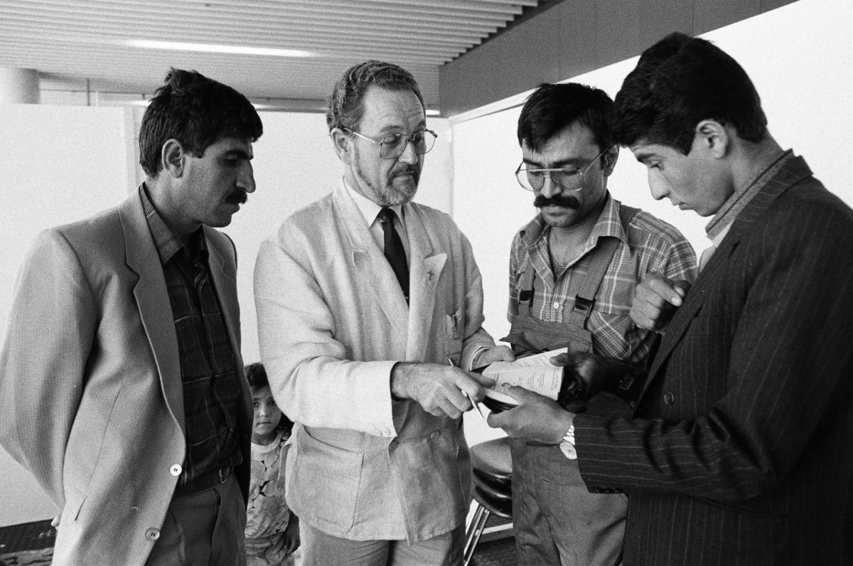 Der evangelische Flughafenpfarrer Karl G. Gutberlet im Gespräch mit Asylbewerbern, 1987. Seit 1971 existierten ein ökumenisches seelsorgerisches Beratungsbüro und eine Kapelle im Flughafen. Vom Ziel, das Evangelium am globalen Transitort zu verkünden, verlagerte sich die Priorität des Pfarrers bald hin zu handfesten sozialen Problemen am Flughafen, einschließlich der Situation von Asylsuchenden. (Milan Skaryd, Fraport AG, Fraport Archiv) Der evangelische Flughafenpfarrer Karl G. Gutberlet im Gespräch mit Asylbewerbern, 1987. Seit 1971 existierten ein ökumenisches seelsorgerisches Beratungsbüro und eine Kapelle im Flughafen. Vom Ziel, das Evangelium am globalen Transitort zu verkünden, verlagerte sich die Priorität des Pfarrers bald hin zu handfesten sozialen Problemen am Flughafen, einschließlich der Situation von Asylsuchenden. (Milan Skaryd, Fraport AG, Fraport Archiv)