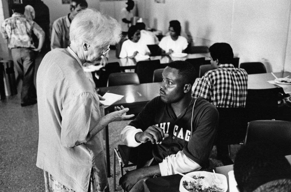 Eine Mitarbeiterin des Flughafensozialdienstes informiert oder berät einen wartenden Asylbewerber. Das Bild von 1993 spiegelt die asymmetrische Situation für Asylbewerber:innen in der 1988 eingerichteten Transitunterkunft wider. (TERZ!/Süddeutsche Zeitung Photo) Eine Mitarbeiterin des Flughafensozialdienstes informiert oder berät einen wartenden Asylbewerber. Das Bild von 1993 spiegelt die asymmetrische Situation für Asylbewerber:innen in der 1988 eingerichteten Transitunterkunft wider. (TERZ!/Süddeutsche Zeitung Photo)