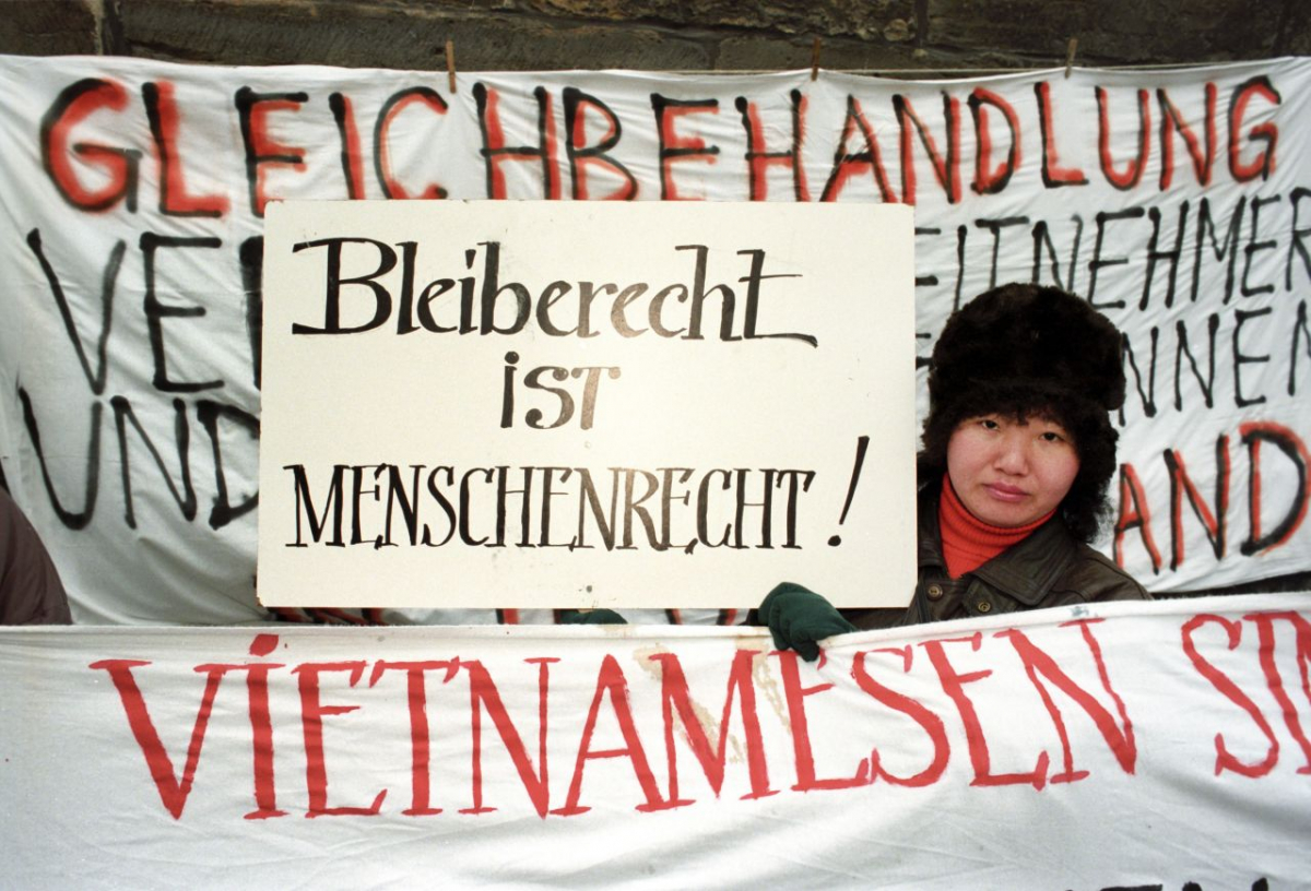 Infolge der deutschen Einheit stellte sich die Frage nach dem Bleiberecht ehemaliger Vertragsarbeiter:innen, die etwa aus Vietnam in die DDR gekommen waren. Das Foto entstand Ende 1995 bei einer Demonstration in Erfurt, die anlässlich der dortigen Innenministerkonferenz von der evangelischen Kirche, dem Ausländer- und Flüchtlingsrat Thüringen sowie Bündnis 90/Die Grünen organisiert wurde. Erst 1997 einigten sich die Innenminister der Länder über permanente Aufenthaltsrechte für ehemalige Vertragsarbeiter:innen, verbunden mit Möglichkeiten zum Familiennachzug. (picture-alliance/ZB/Ralf Hirschberger) Infolge der deutschen Einheit stellte sich die Frage nach dem Bleiberecht ehemaliger Vertragsarbeiter:innen, die etwa aus Vietnam in die DDR gekommen waren. Das Foto entstand Ende 1995 bei einer Demonstration in Erfurt, die anlässlich der dortigen Innenministerkonferenz von der evange- lischen Kirche, dem Ausländer- und Flüchtlingsrat Thüringen sowie Bündnis 90/Die Grünen organisiert wurde. Erst 1997 einigten sich die Innenminister der Länder über permanente Aufenthaltsrechte für ehemalige Vertragsarbeiter:innen, verbunden mit Möglichkeiten zum Familiennachzug. (picture-alliance/ZB/Ralf Hirschberger)