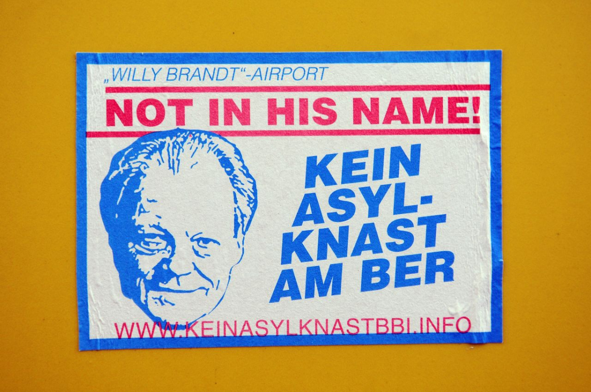 Aufkleber aus Protest gegen ein Abschiebegefängnis, Oktober 2012. Von 2006 bis 2020 wurde der Flughafen Berlin Brandenburg gebaut; Ende 2009 fiel die Entscheidung, »Willy Brandt« als Beinamen zu verwenden. Im Namen Brandts, der während der NS-Zeit im skandinavischen Exil gewesen war, dürfe es keinen »Asyl-Knast« am Flughafen geben – so das geschichtspolitische Argument des Protests. Die Protestierenden waren sich jedoch nicht bewusst, dass auch unter dem Bundeskanzler Brandt (SPD) Abschiebepraktiken und -haft weiterentwickelt und vorangetrieben wurden. (picture-alliance/zb/Matthias Tödt) Aufkleber aus Protest gegen ein Abschiebegefängnis, Oktober 2012. Von 2006 bis 2020 wurde der Flughafen Berlin Brandenburg gebaut; Ende 2009 fiel die Entscheidung, »Willy Brandt« als Beinamen zu verwenden. Im Namen Brandts, der während der NS-Zeit im skandinavischen Exil gewesen war, dürfe es keinen »Asyl-Knast« am Flughafen geben – so das geschichtspolitische Argument des Protests. Die Protestierenden waren sich jedoch nicht bewusst, dass auch unter dem Bundeskanzler Brandt (SPD) Abschiebepraktiken und -haft weiterentwickelt und vorangetrieben wurden. (picture-alliance/zb/Matthias Tödt)